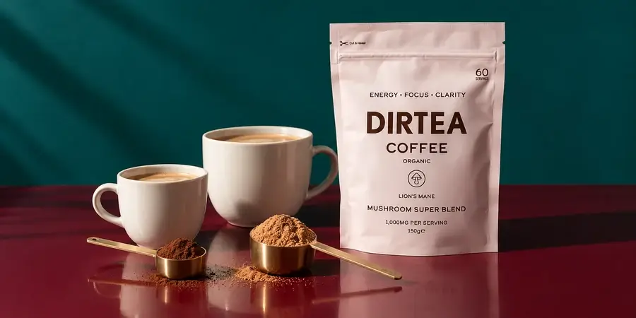 Pouch of Dirtea Coffee beside a small and a large scoop of powder and two cups of coffee on a burgundy table