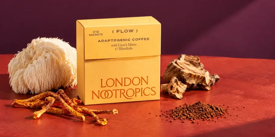 Box of London Nootropics Flow coffee beside a lion's mane mushroom, dried cordyceps, rhodiola root and instant coffee on a red table