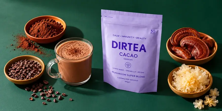 Pouch of Dirtea Cacao beside a glass of hot chocolate, cocoa powder, cacao nibs, reishi and tremella on a dark green background