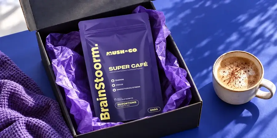 Open delivery box holding a purple Brainstoorm pouch on violet tissue paper, with a cappuccino dusted with cocoa on a blue table