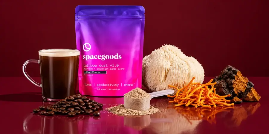 Bag of Spacegoods Rainbow Dust with a glass mug of coffee, coffee beans, a scoop of powder, lion's mane, cordyceps and chaga on a burgundy background